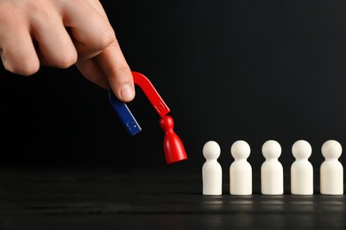 Photo of Man with magnet attracting red piece among wooden ones at black table, closeup