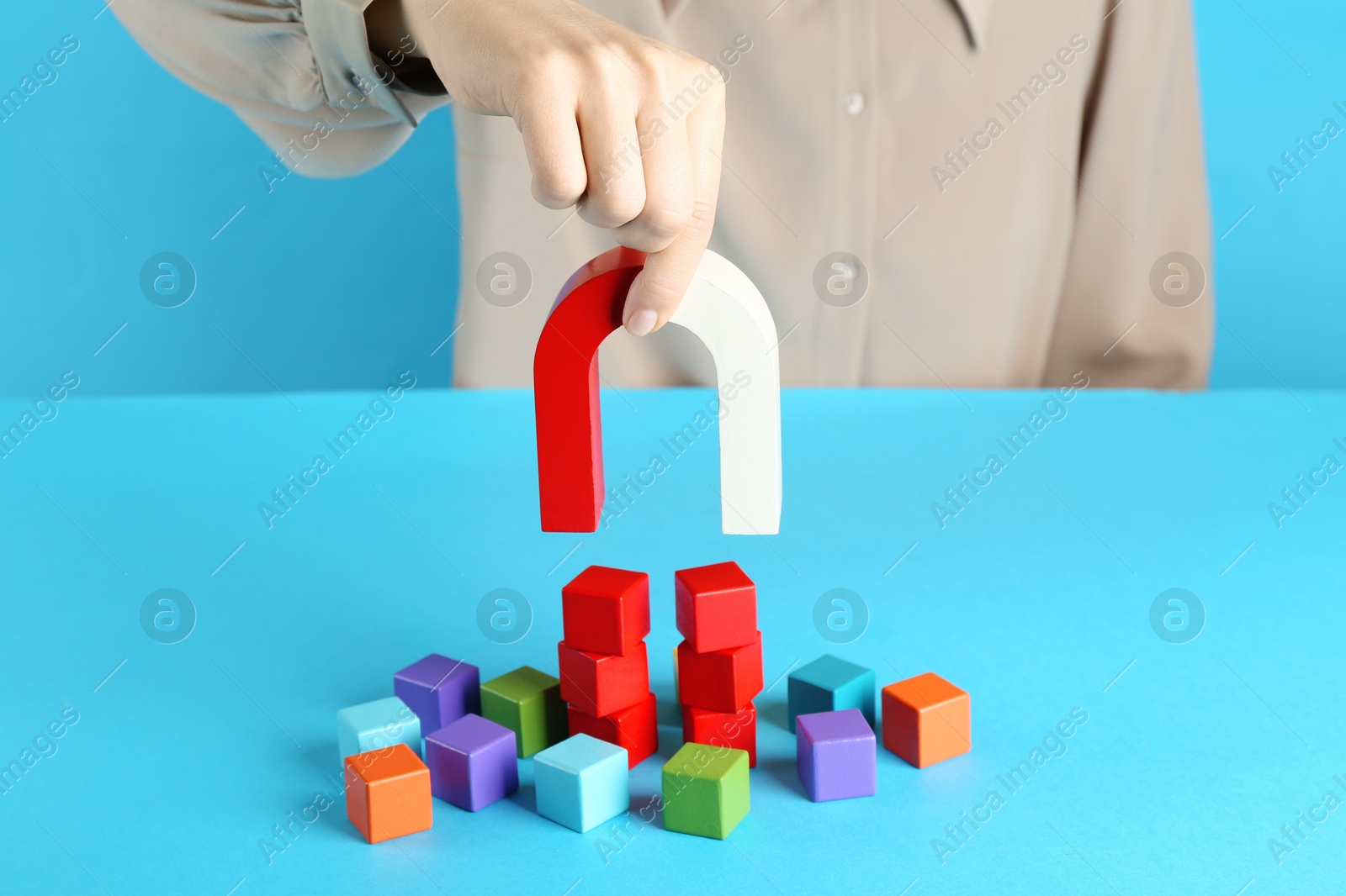 Photo of Woman with magnet attracting colorful cubes on light blue background, closeup