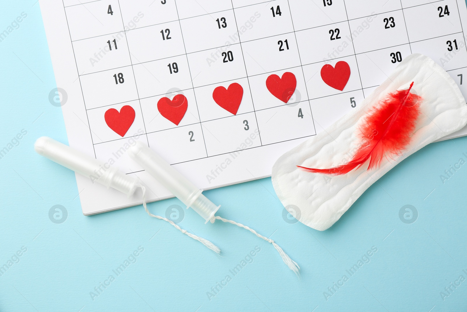 Photo of Calendar with marked dates, menstrual pad with feather and tampons on light blue background, top view