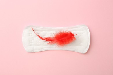 Photo of Menstrual pad with red feather on light pink background, top view