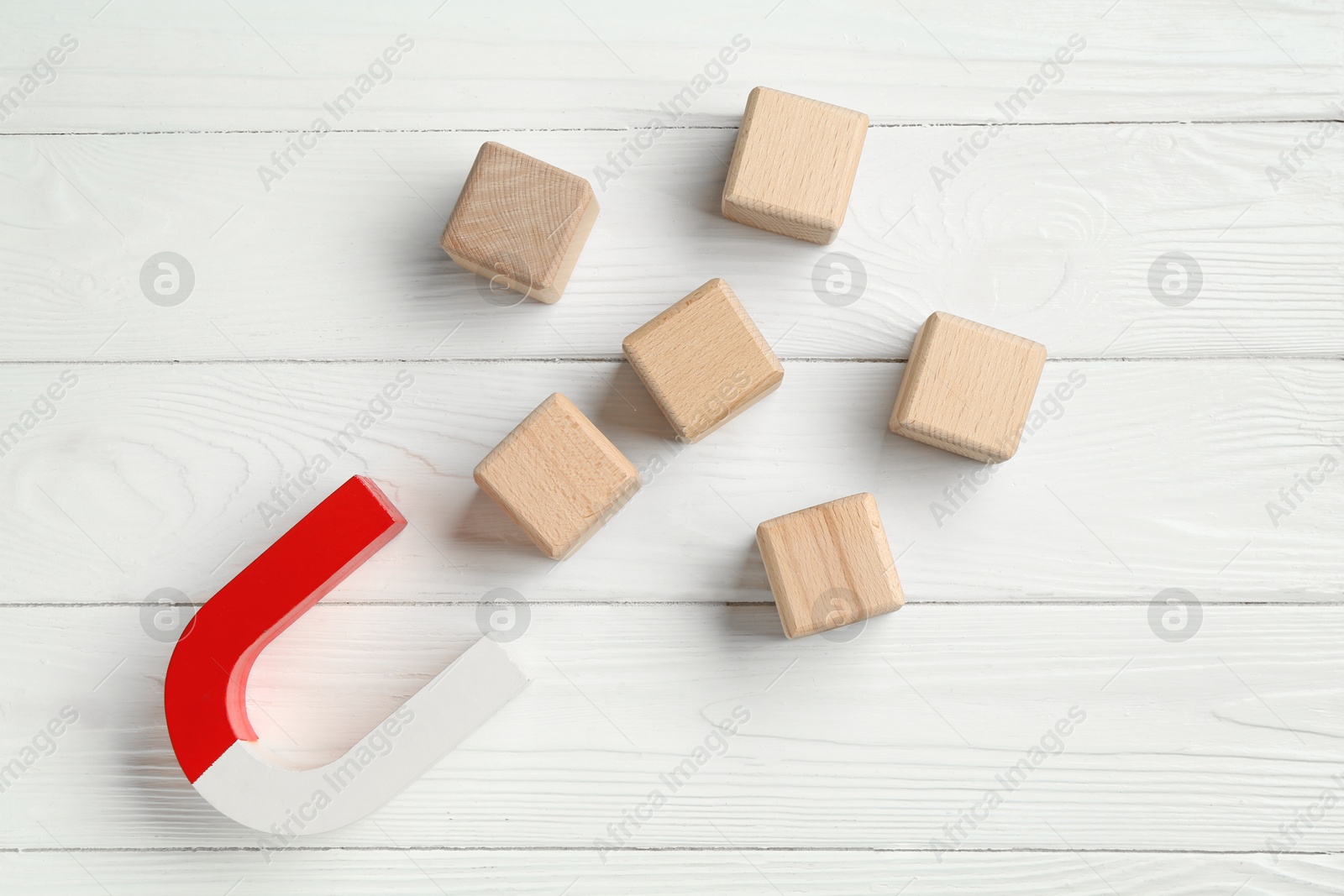 Photo of Magnet attracting cubes on white wooden table, flat lay