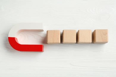 Photo of Magnet attracting cubes on white wooden table, flat lay