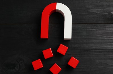 Photo of Magnet attracting red cubes on black wooden table, flat lay