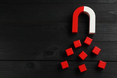 Photo of Magnet attracting red cubes on black wooden table, flat lay