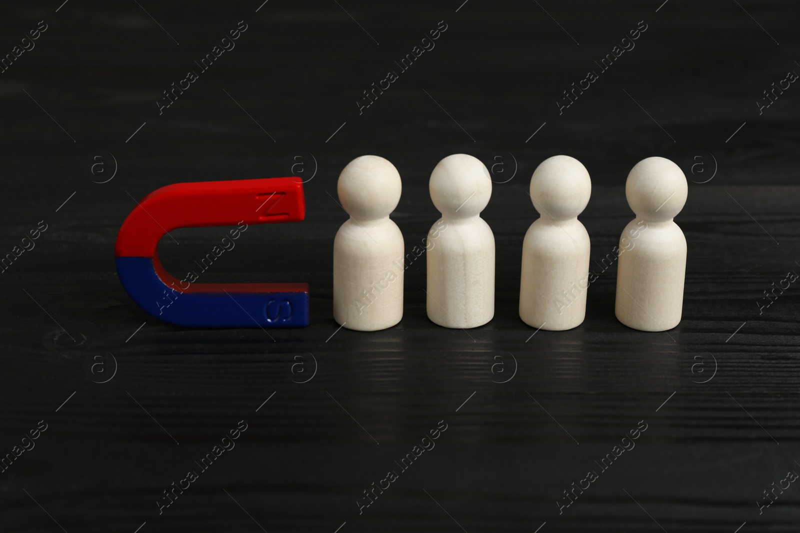 Photo of Magnet attracting human figures on black wooden table