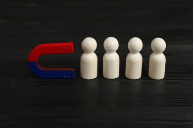 Photo of Magnet attracting human figures on black wooden table