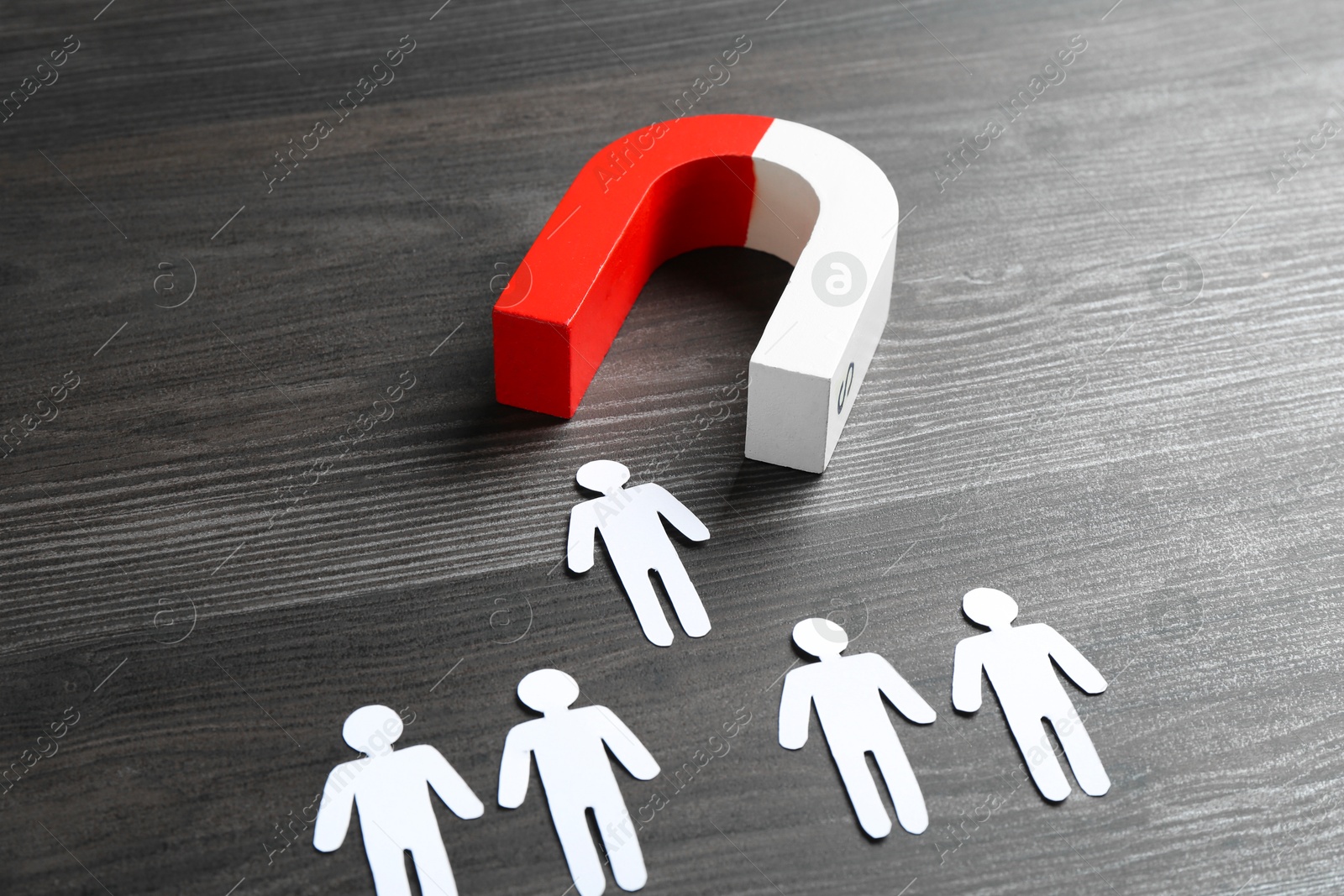 Photo of Magnet attracting paper human figures on wooden table, closeup