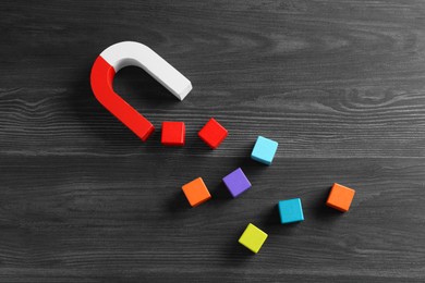 Photo of Magnet attracting with colorful cubes on wooden table, flat lay