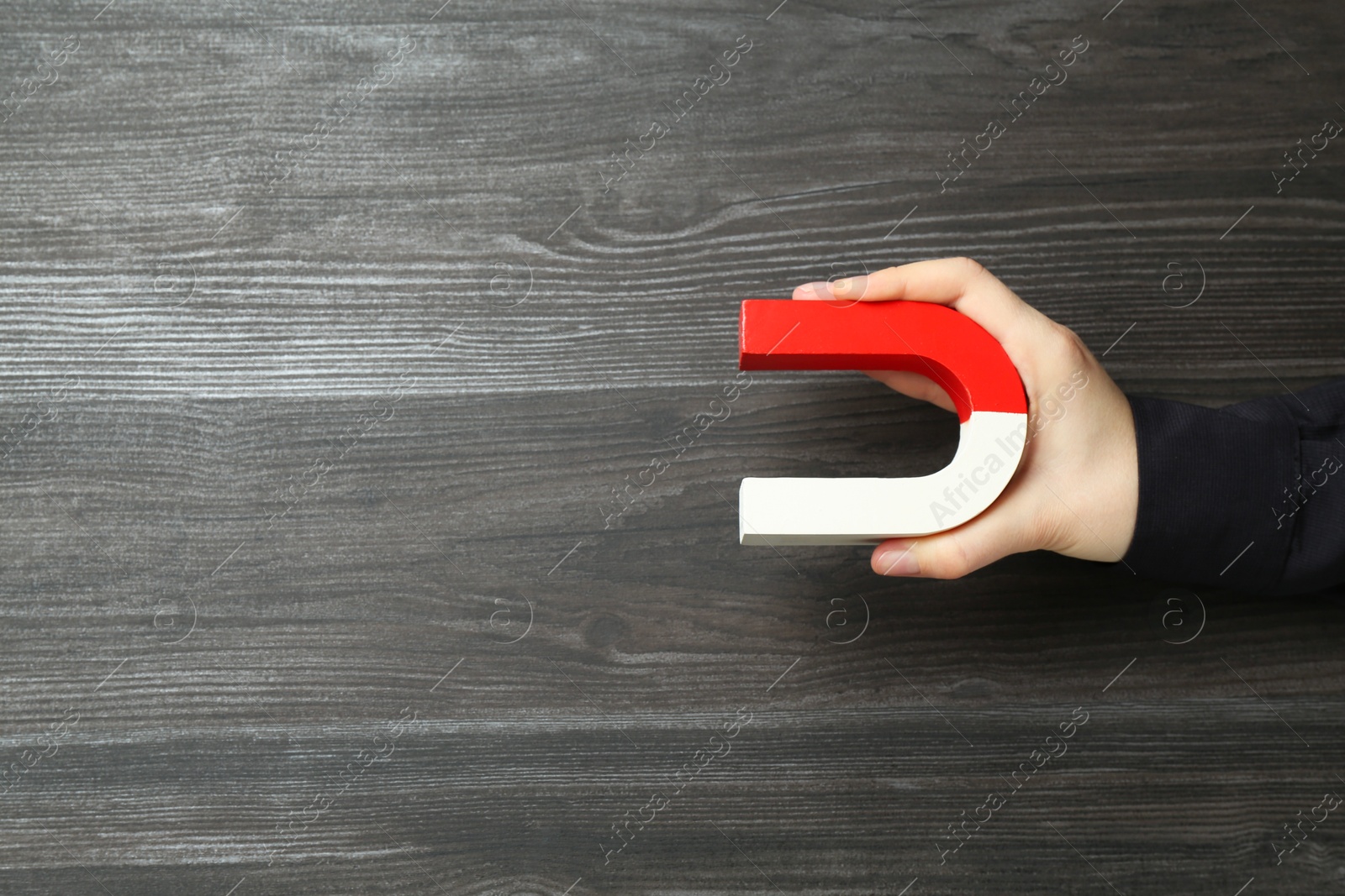 Photo of Woman with horseshoe magnet on wooden background, top view. Space for text