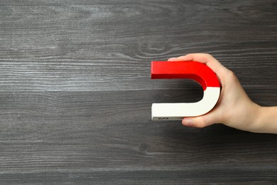 Photo of Woman with horseshoe magnet on wooden background, top view. Space for text