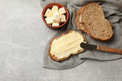 Photo of Fresh bread with butter and knife on grey table, flat lay. Space for text