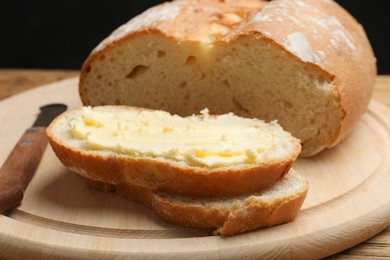 Photo of Fresh bread with butter and knife on wooden table, closeup