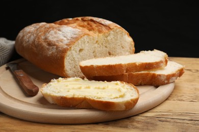 Photo of Fresh bread with butter and knife on wooden table, closeup