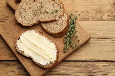 Photo of Fresh bread with butter and thyme on wooden table, top view. Space for text