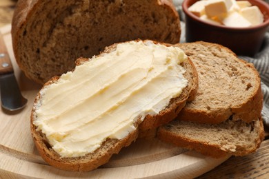 Photo of Fresh bread with butter and knife on wooden table, closeup