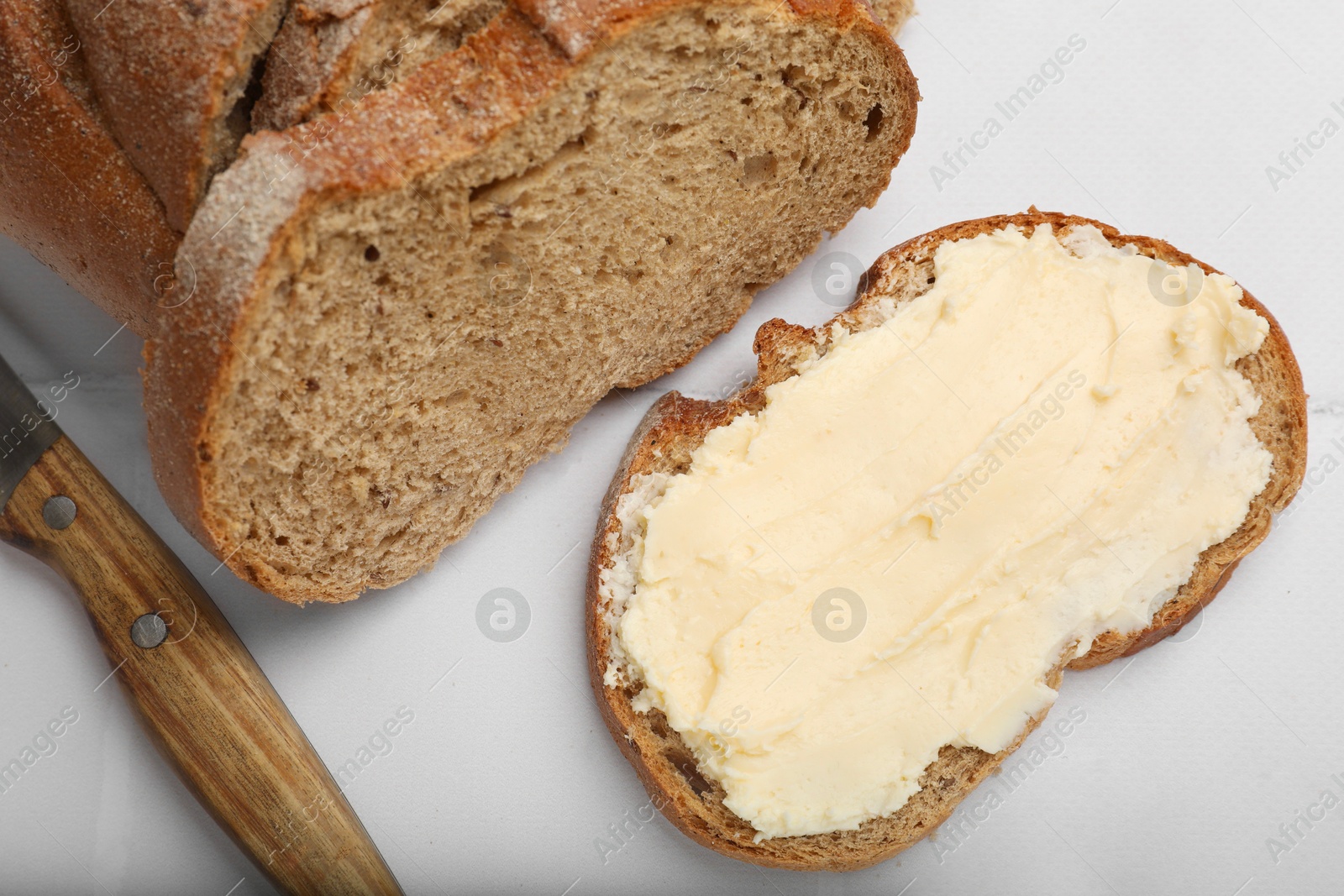 Photo of Fresh bread with butter and knife on white tiled table, top view