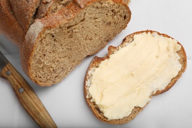 Photo of Fresh bread with butter and knife on white tiled table, top view