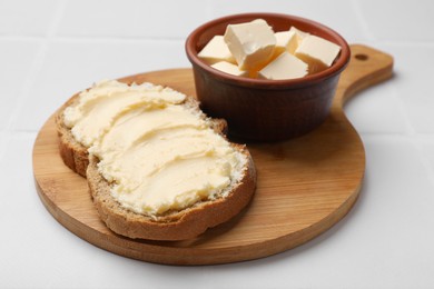 Photo of Fresh bread with butter on white tiled table, closeup