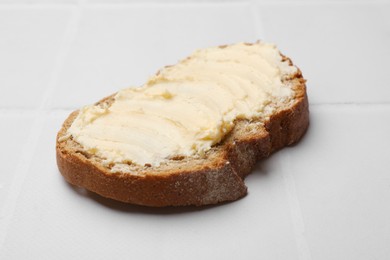 Photo of Fresh bread with butter on white tiled table, closeup