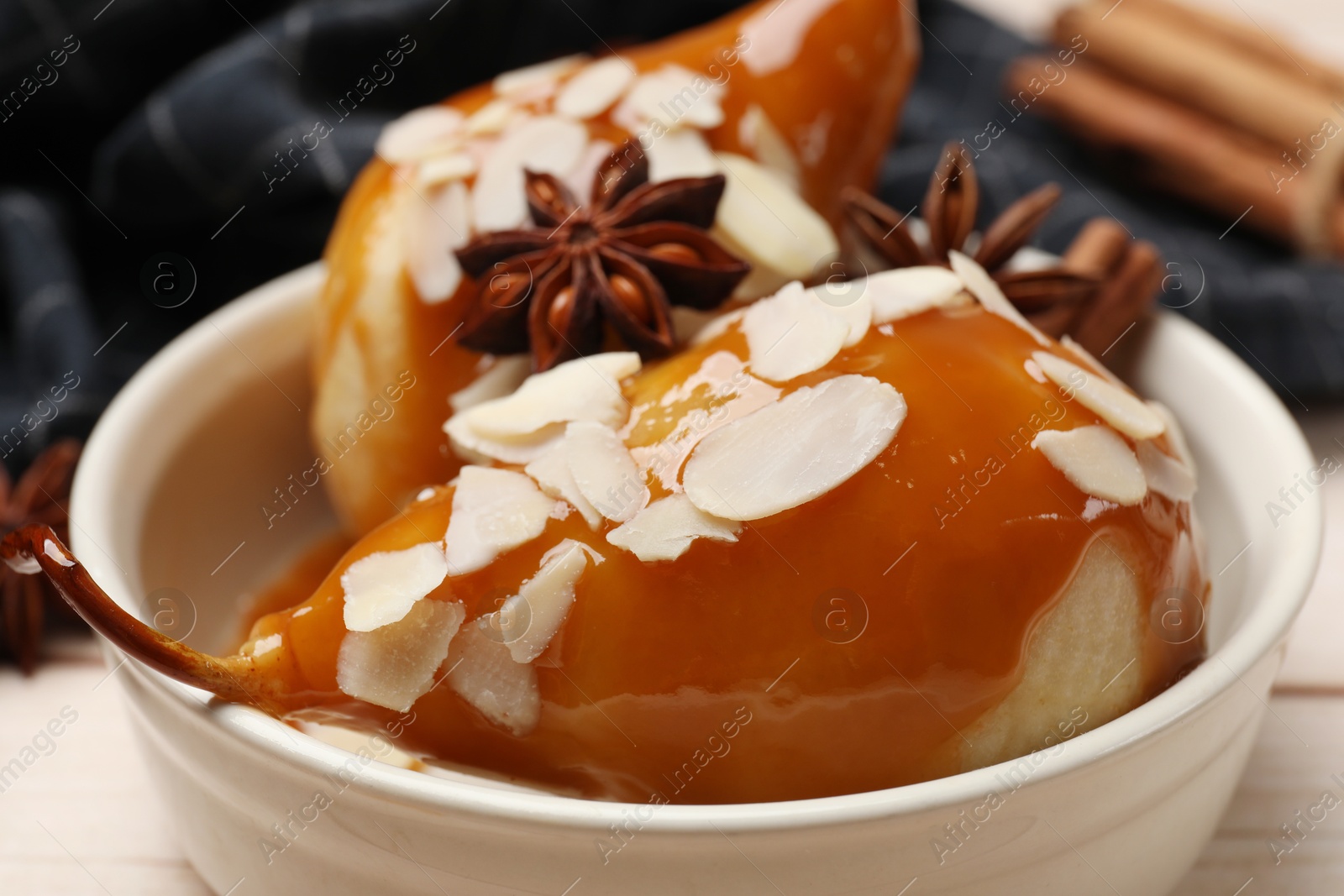 Photo of Delicious pears with caramel sauce, almond flakes and spices on white wooden table, closeup