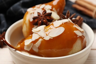 Delicious pears with caramel sauce, almond flakes and spices on white wooden table, closeup