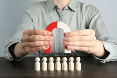 Photo of Woman with magnet attracting human figures at wooden table, closeup