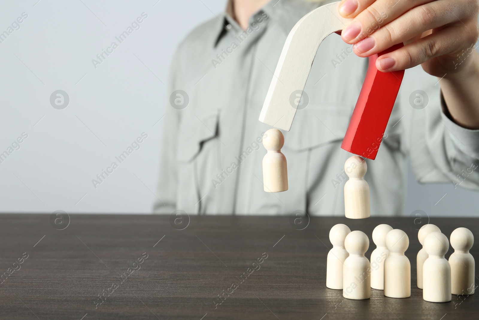 Photo of Woman with magnet attracting human figures at wooden table, closeup. Space for text