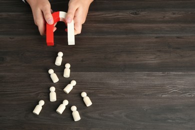 Photo of Man with magnet attracting human figures at wooden table, above view. Space for text