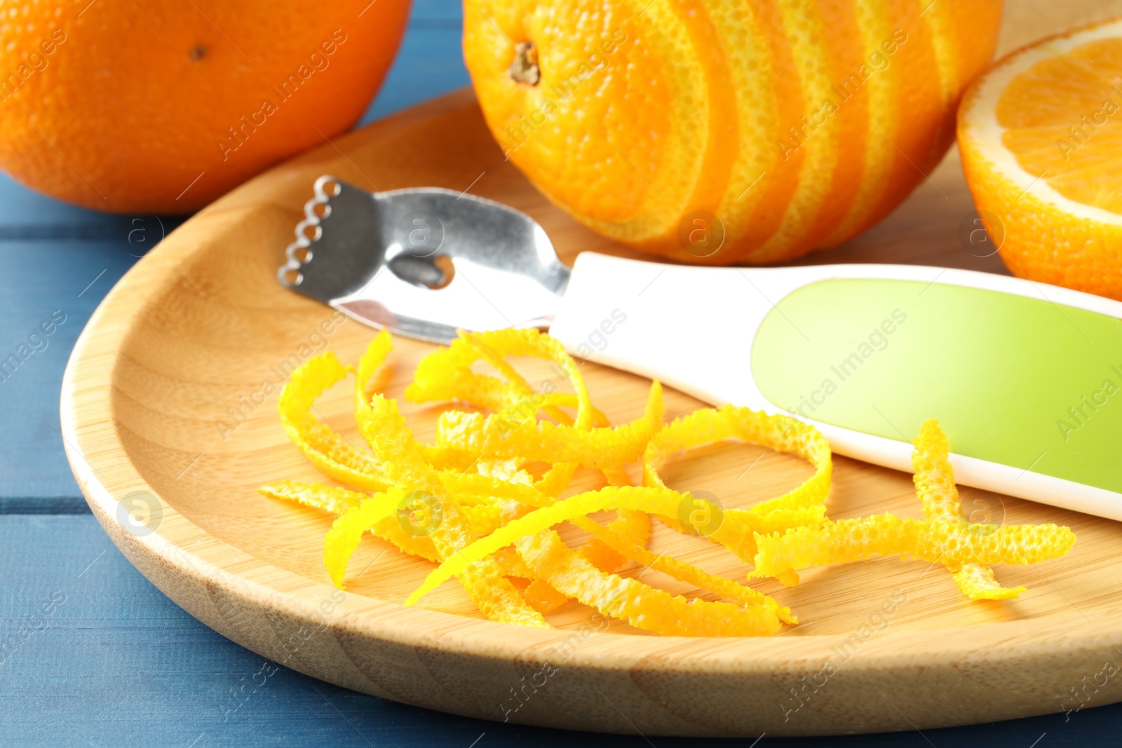 Photo of Plate with orange zest, fresh fruit and zester on blue wooden table, closeup