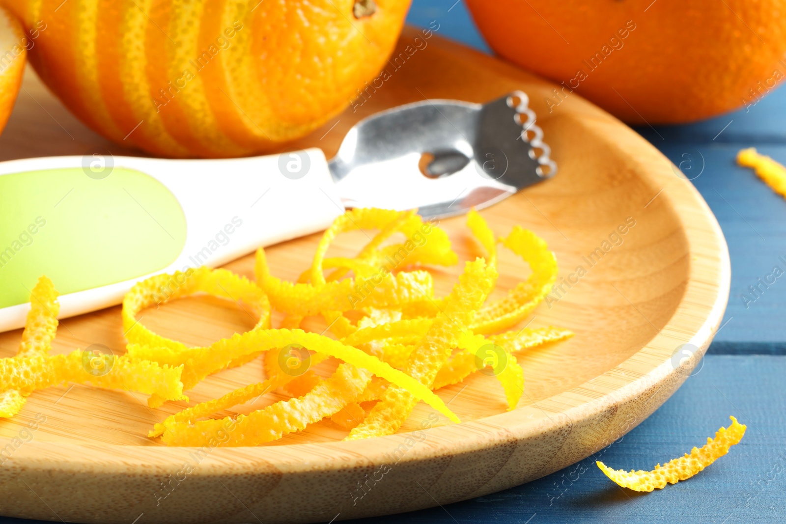 Photo of Plate with orange zest, fresh fruit and zester on blue wooden table, closeup