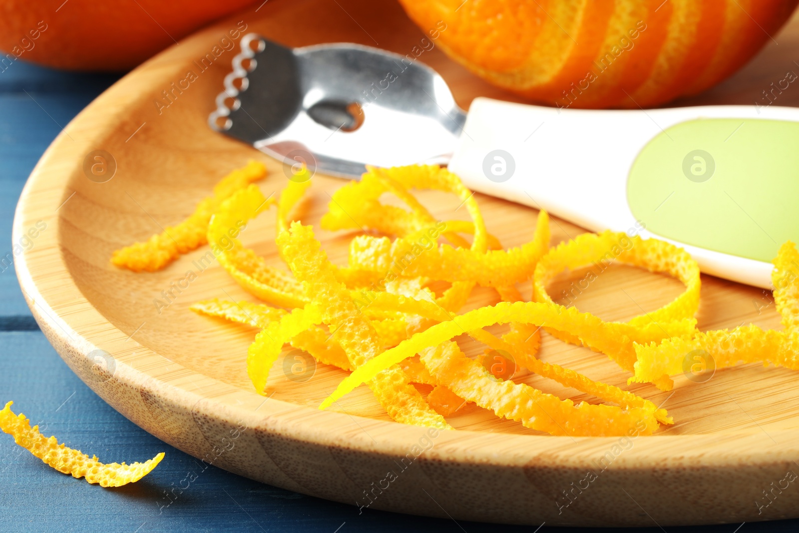 Photo of Plate with orange zest, fresh fruit and zester on blue wooden table, closeup