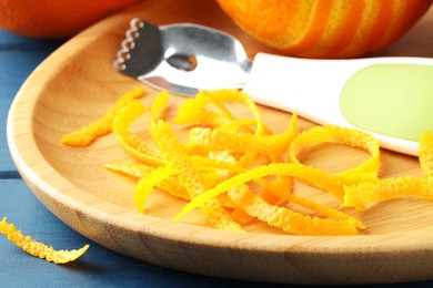 Photo of Plate with orange zest, fresh fruit and zester on blue wooden table, closeup