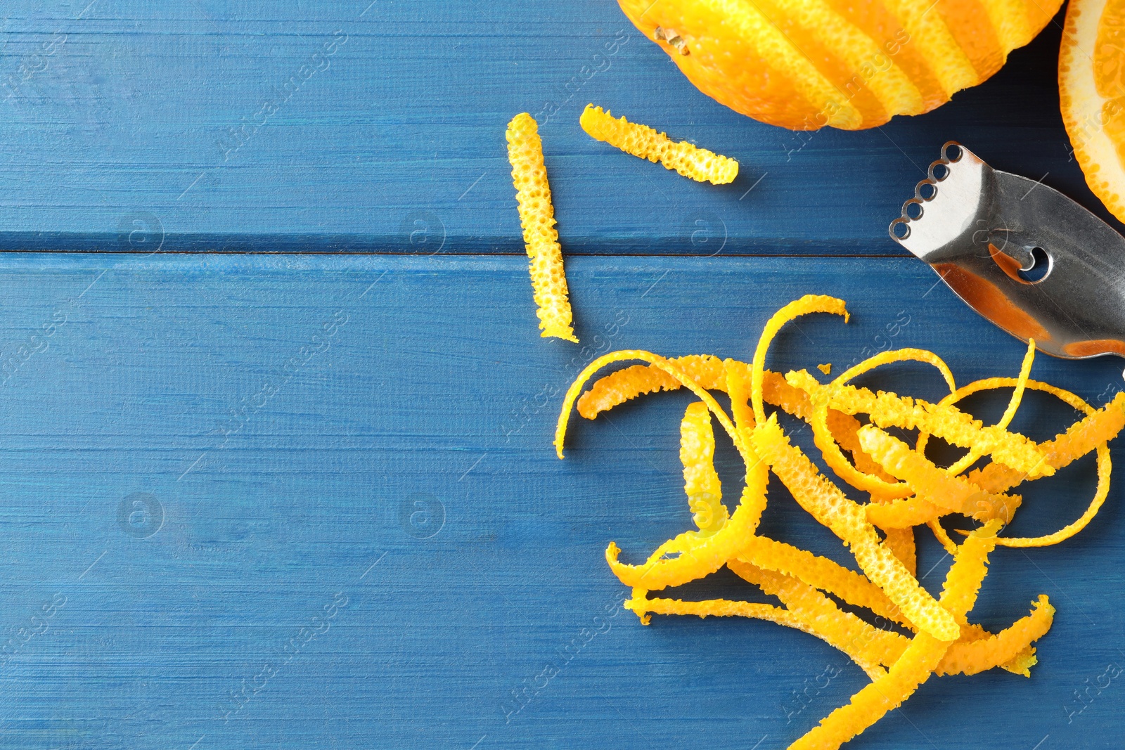 Photo of Fresh orange zest, fruits and zester on blue wooden table, flat lay. Space for text