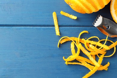 Photo of Fresh orange zest, fruits and zester on blue wooden table, flat lay. Space for text