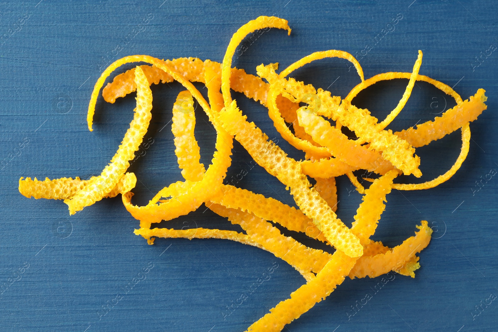 Photo of Pile of fresh orange zest on blue wooden table, top view