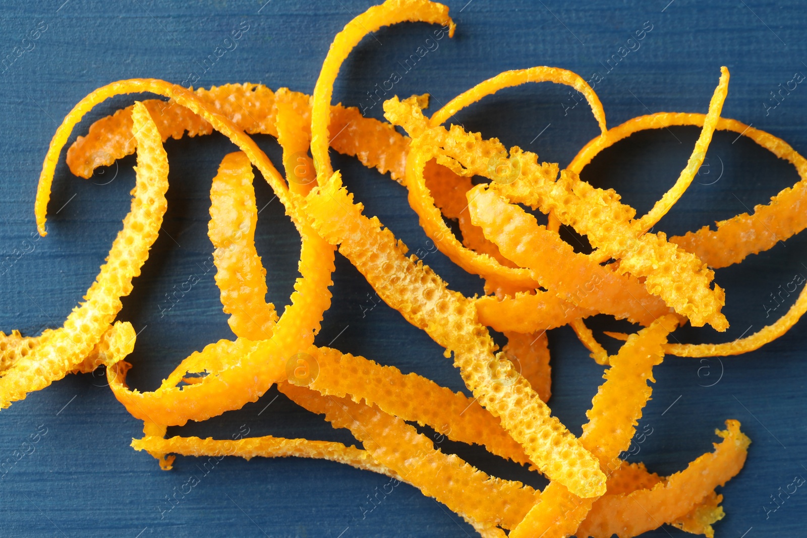 Photo of Pile of fresh orange zest on blue wooden table, top view