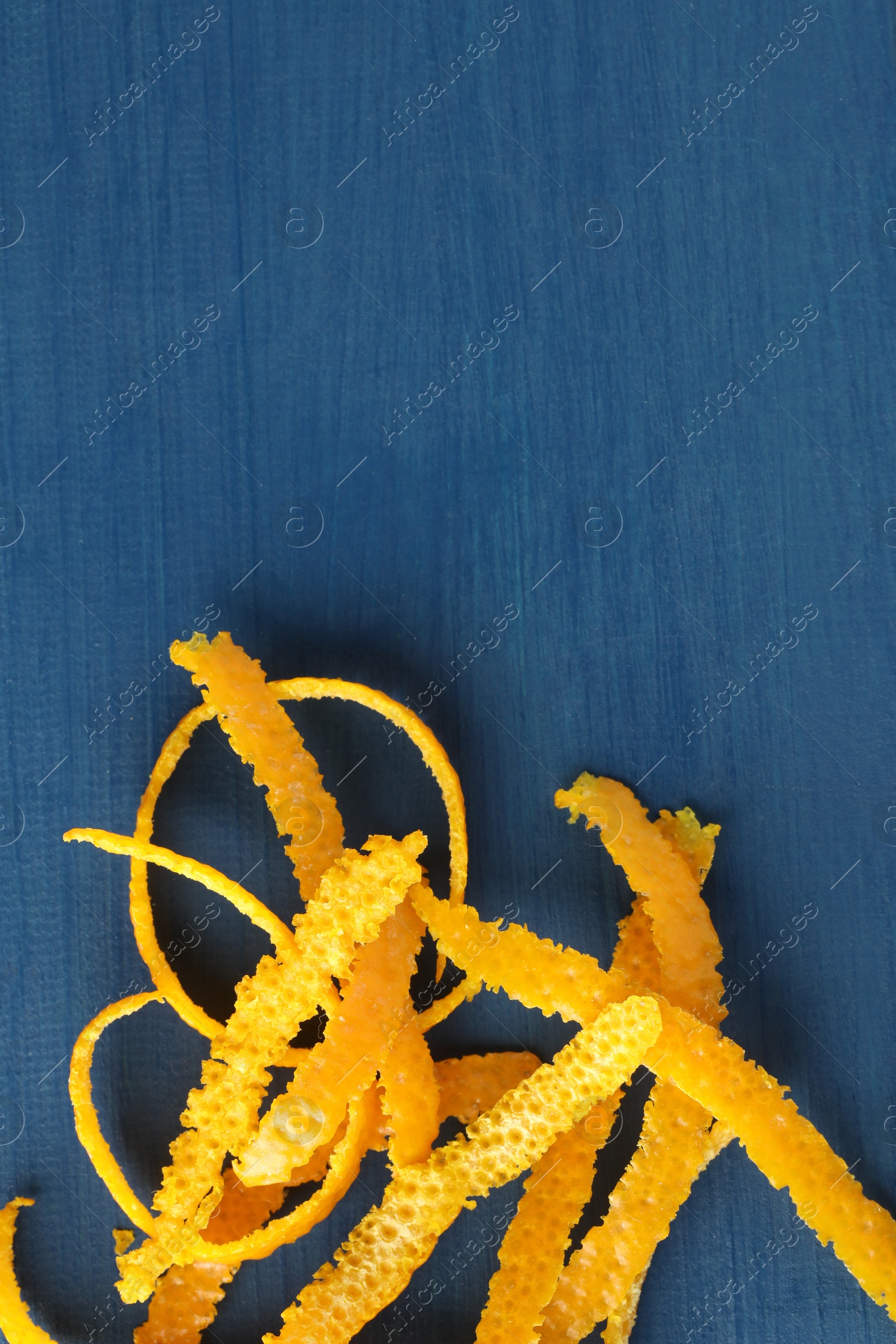 Photo of Pile of fresh orange zest on blue wooden table, top view. Space for text