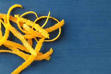 Photo of Pile of fresh orange zest on blue wooden table, top view. Space for text