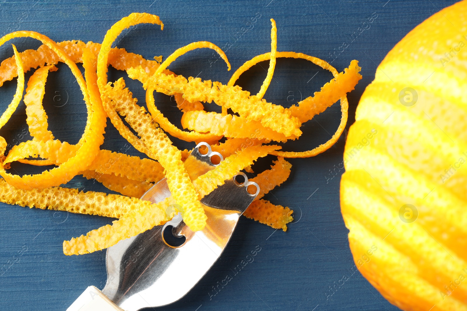 Photo of Fresh orange zest, fruit and zester on blue wooden table, flat lay