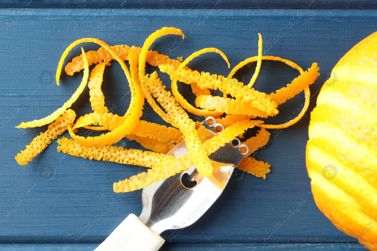 Photo of Fresh orange zest, fruit and zester on blue wooden table, flat lay