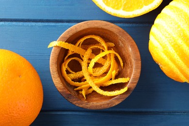 Photo of Bowl with fresh orange zest and fruits on blue wooden table, flat lay