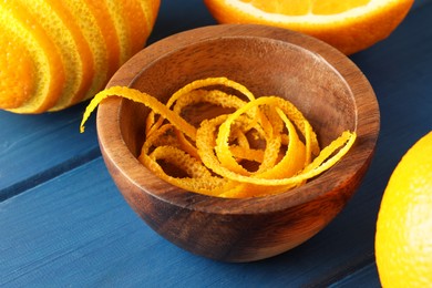 Photo of Bowl with fresh orange zest and fruits on blue wooden table, closeup