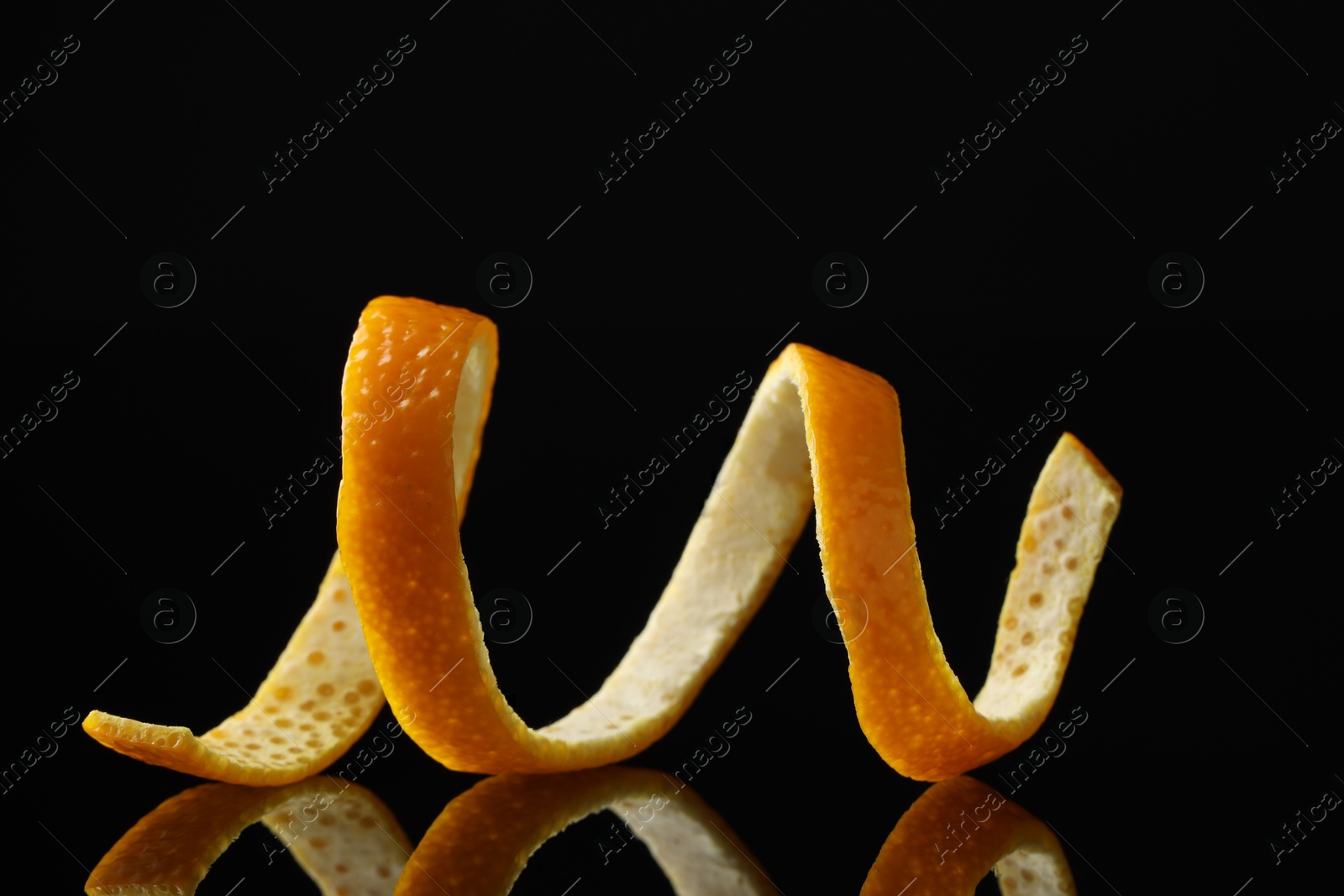 Photo of One fresh orange peel on black mirror surface, closeup