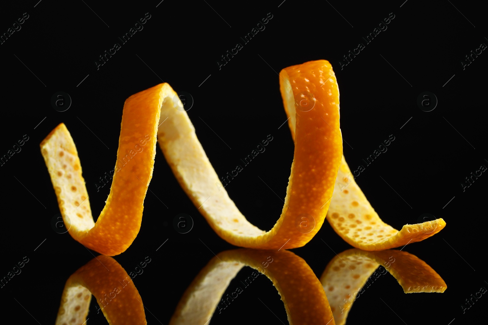 Photo of One fresh orange peel on black mirror surface, closeup