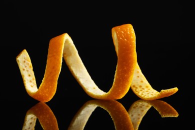 Photo of One fresh orange peel on black mirror surface, closeup