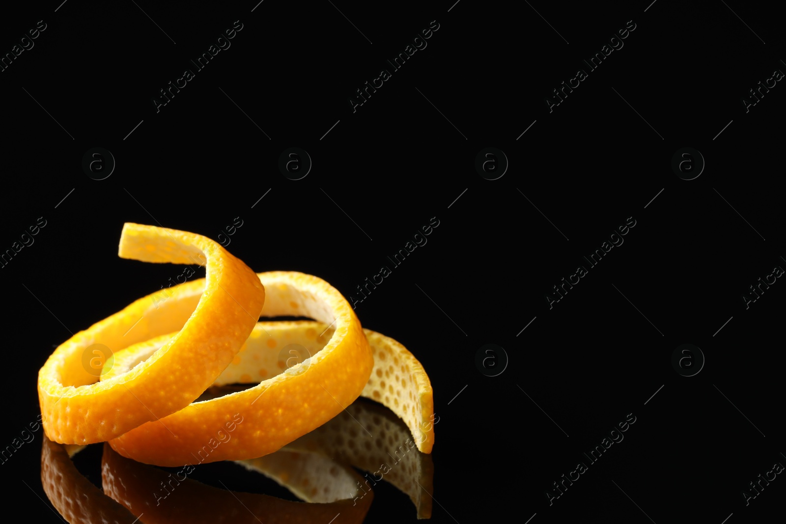 Photo of One fresh orange peel on black mirror surface, closeup. Space for text