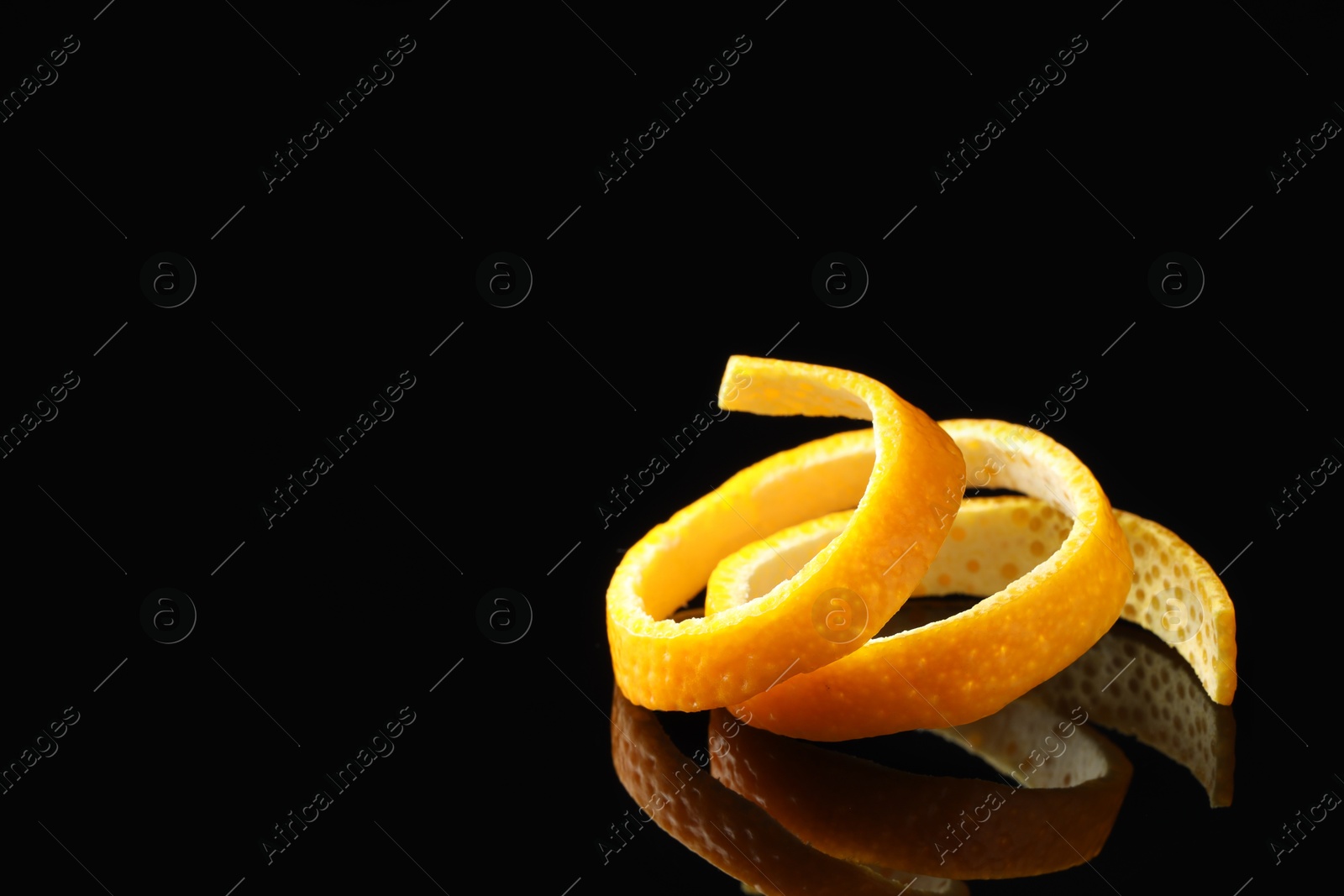 Photo of One fresh orange peel on black mirror surface, closeup. Space for text