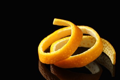 Photo of One fresh orange peel on black mirror surface, closeup. Space for text