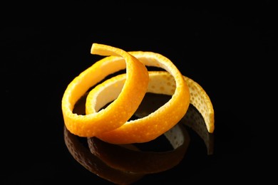 Photo of One fresh orange peel on black mirror surface, closeup