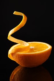 Photo of Fresh orange peel and half of fruit on black mirror surface, closeup